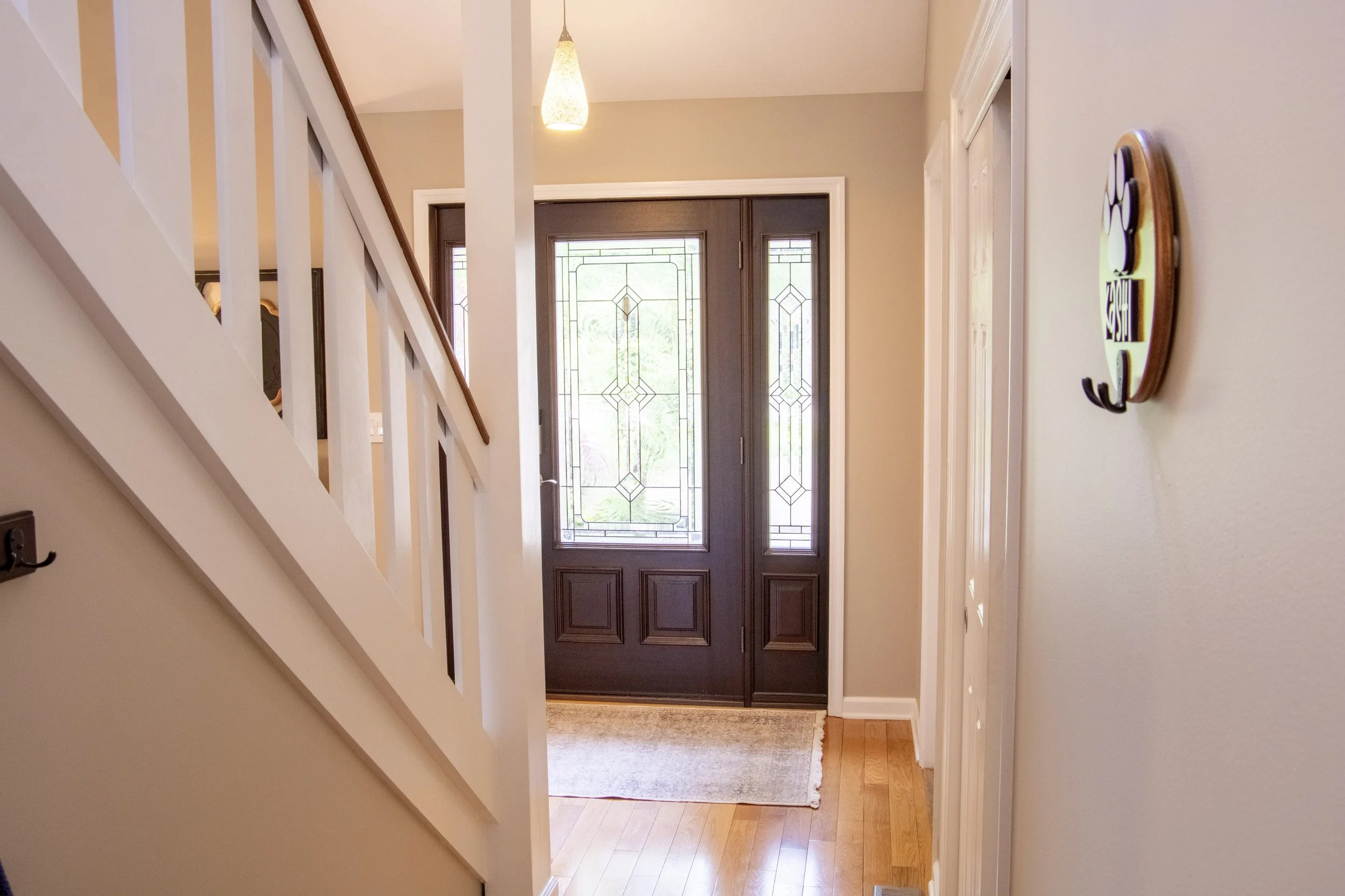 Entryway with a front door, glass panels, and a hallway with hardwood flooring and a beige rug.