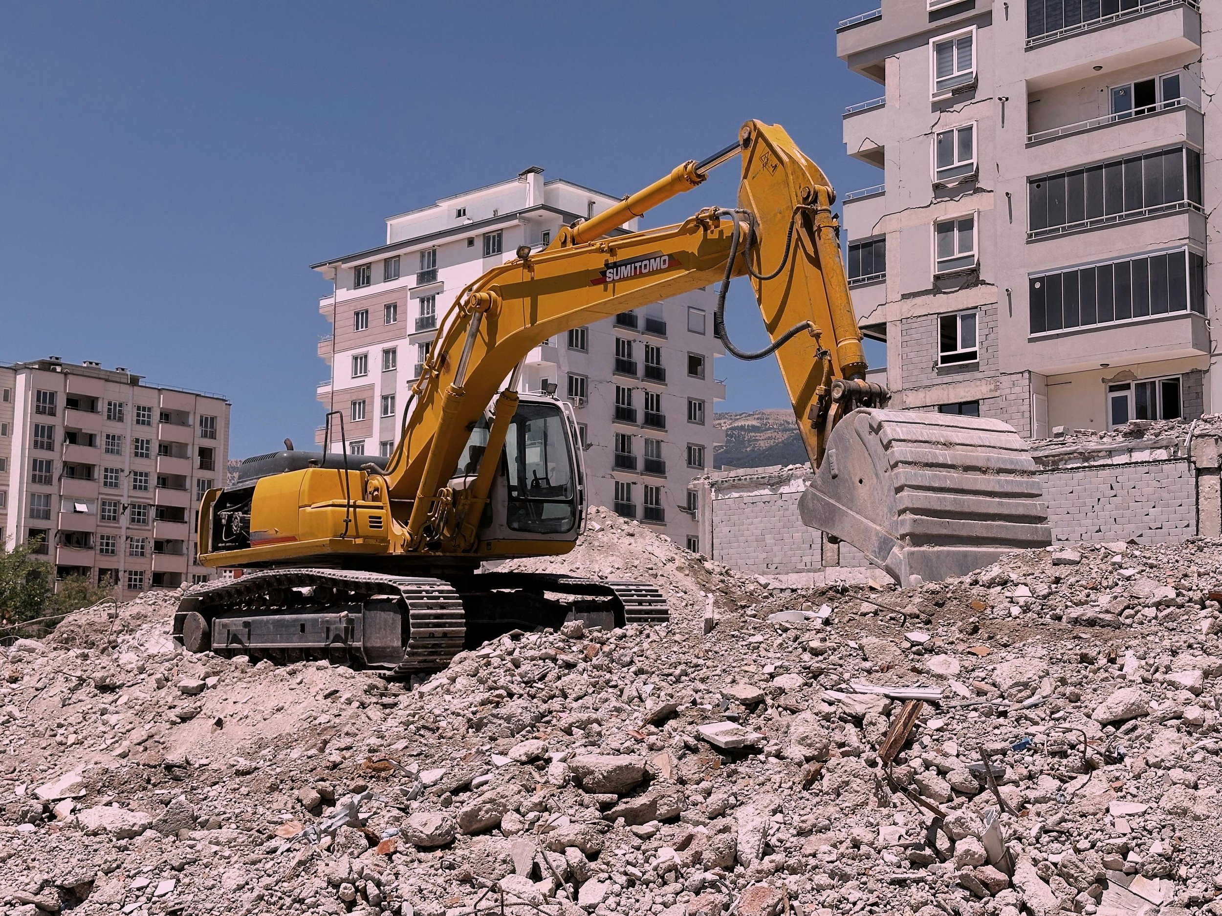Construction site with a yellow excavator moving dirt in front of apartment buildings.