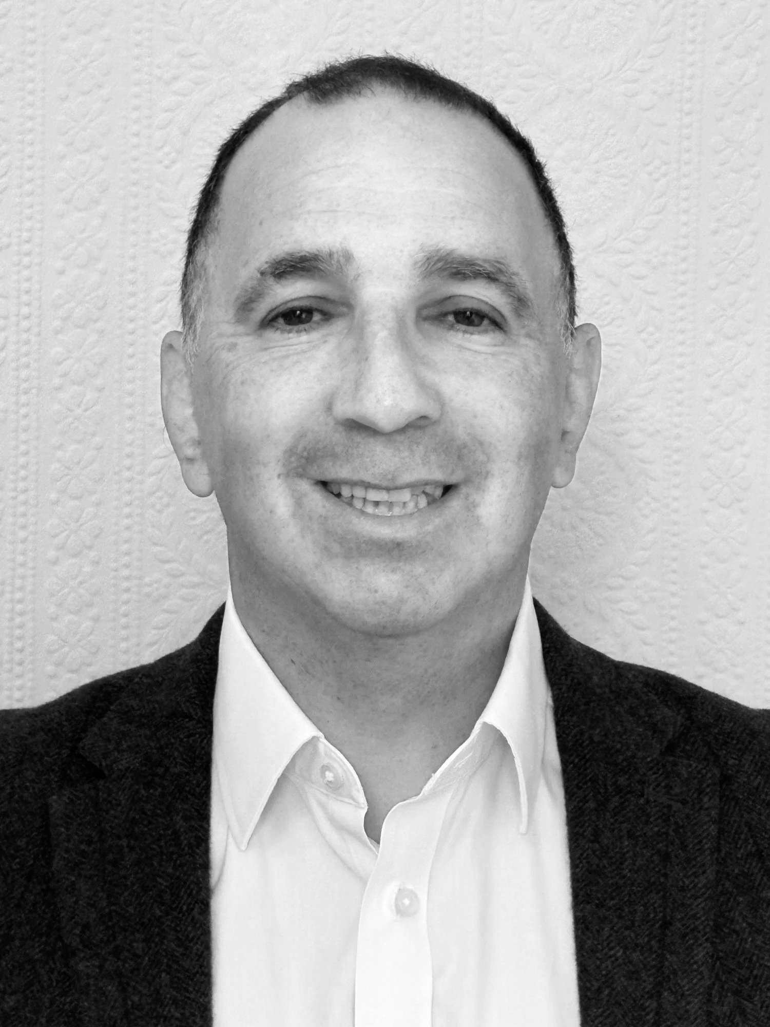 Black and white portrait of a smiling man in a suit, white shirt, and blazer with a textured wall background.