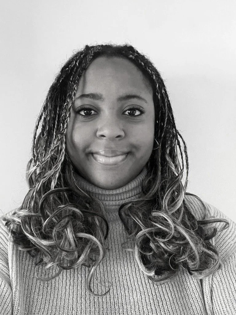 A smiling woman with curly hair, wearing a turtleneck sweater, looking at the camera, in a black and white photo.