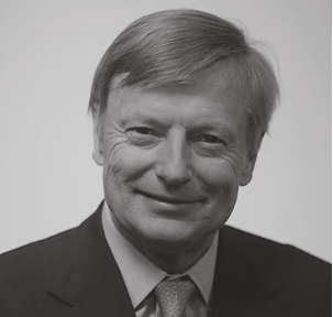 Black and white portrait of a smiling man in a suit and tie with short, light-colored hair.