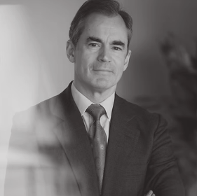 A middle-aged man wearing a suit and tie, looking thoughtfully to the side in a professional setting.