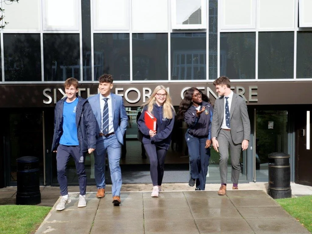 Group of five students walking out of a building labeled 'SIXTH FORM CENTRE' on a busy day.
