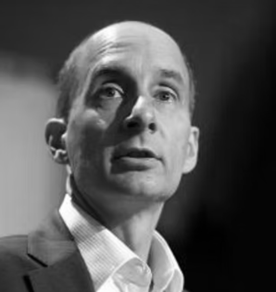 Black and white photograph of a man with slicked-back hair wearing a suit and white shirt, facing slightly to the left.