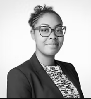 Black and white portrait of a woman wearing glasses, a blazer, and a patterned top, looking at the camera with a confident expression.
