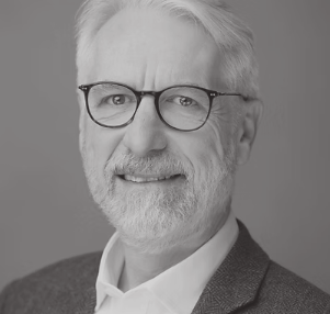Black and white portrait of an older man with white hair and beard, wearing glasses and a suit jacket.