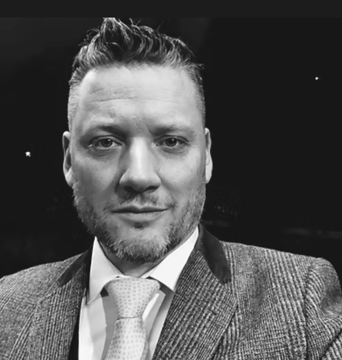 Black and white portrait of a man with short, styled hair, a beard, wearing a suit jacket, shirt, and tie.
