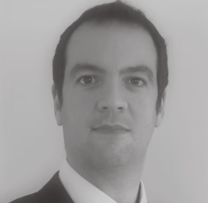 Black-and-white portrait of a man with dark hair, wearing a suit and tie, looking directly at the camera.