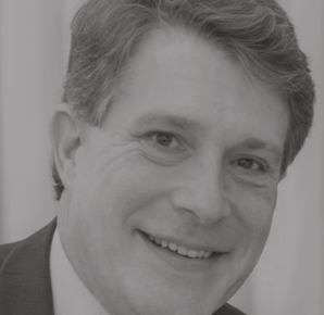 Black and white photo of a smiling man with short hair, wearing a suit.