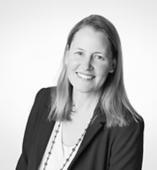 Black and white portrait of a smiling woman with shoulder-length hair, wearing a blazer and necklace.