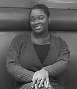 A woman smiling, sitting with her hands on her lap, in a black and white photo.