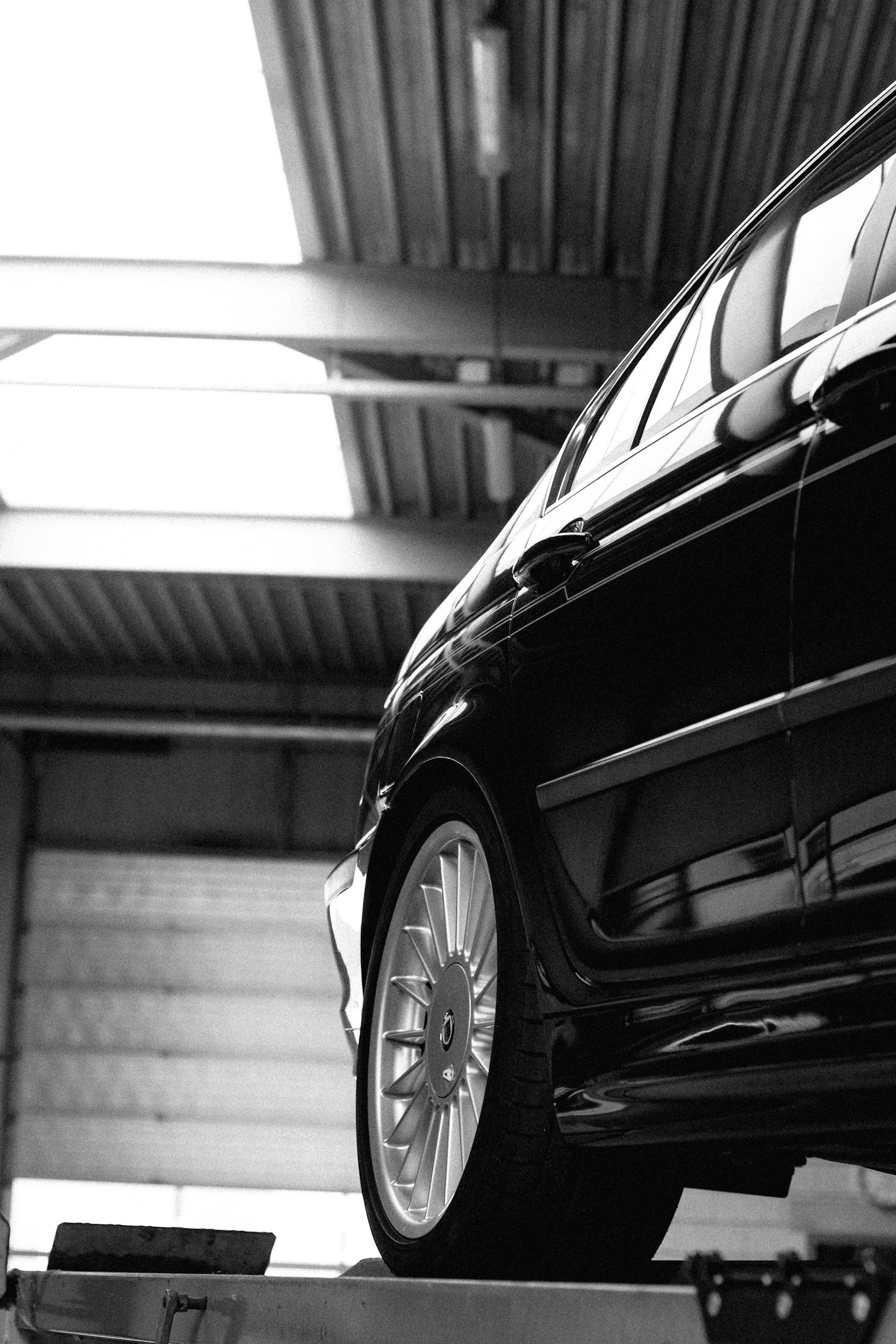 A black luxury car parked in an indoor parking garage with a metallic roof structure.