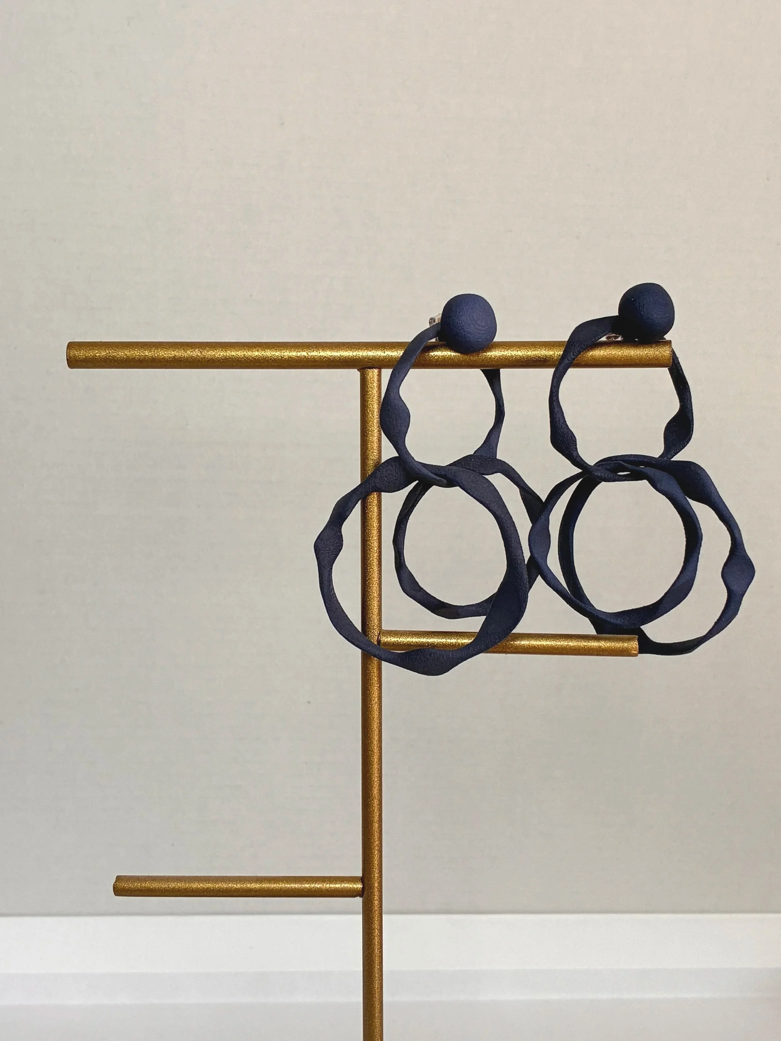 Une paire de lunettes de soleil avec une monture en forme de cercles géants suspendue sur un support en forme de ciseaux doré, contre un fond gris clair.