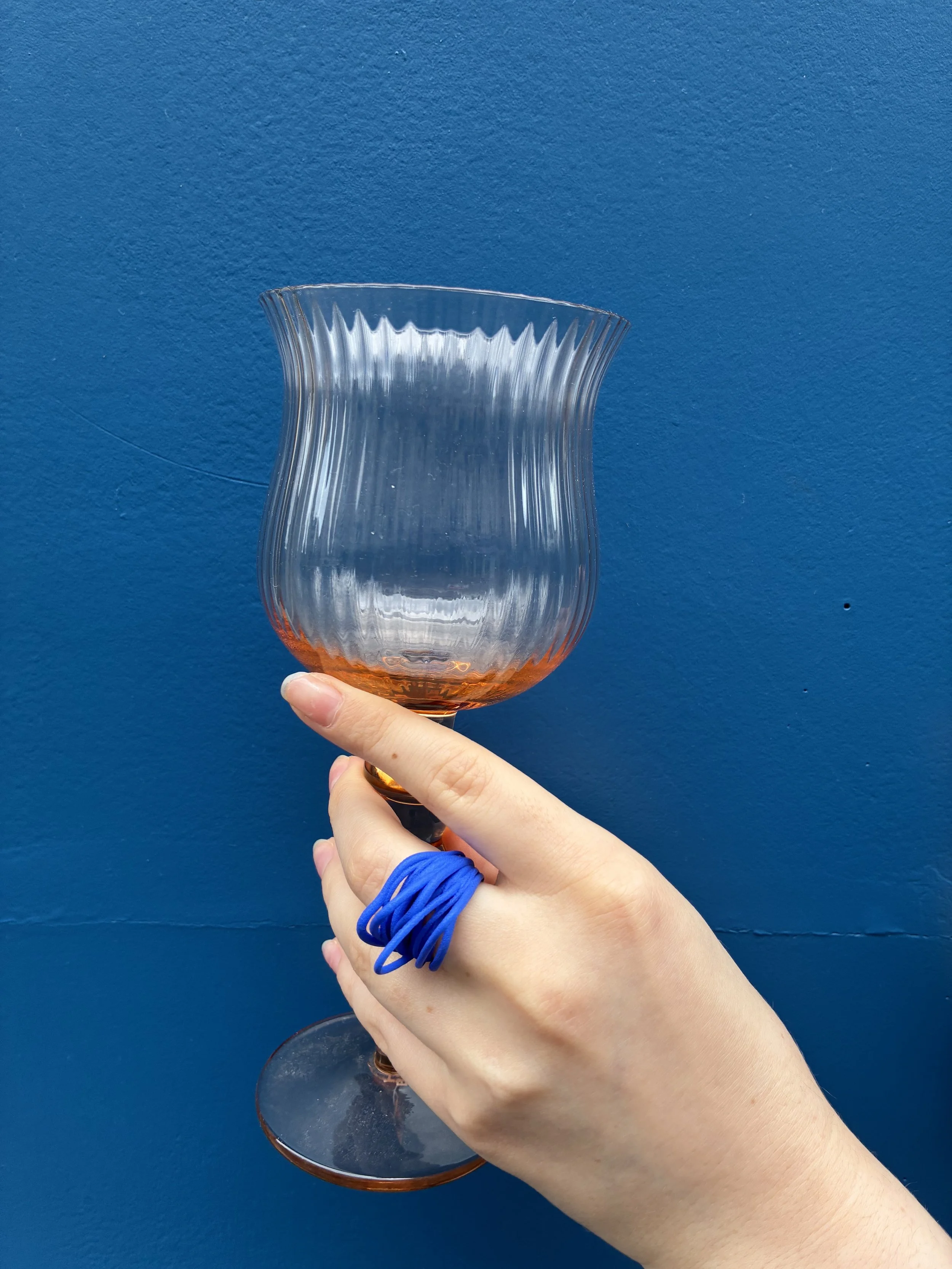 Une main tient un verre en verre transparent avec un fond bleu. Le verre a une forme ondulée avec des rainures verticales.