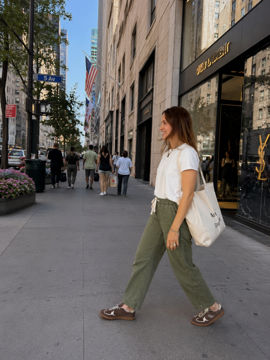 A woman walking on a city sidewalk next to a luxury store, with people and skyscrapers in the background, in New York City.