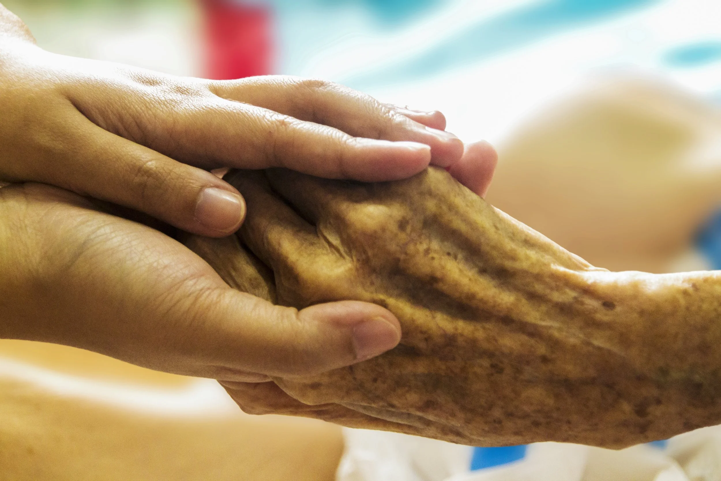 Close-up of a caregiver's hands gently holding an elderly person's hands.