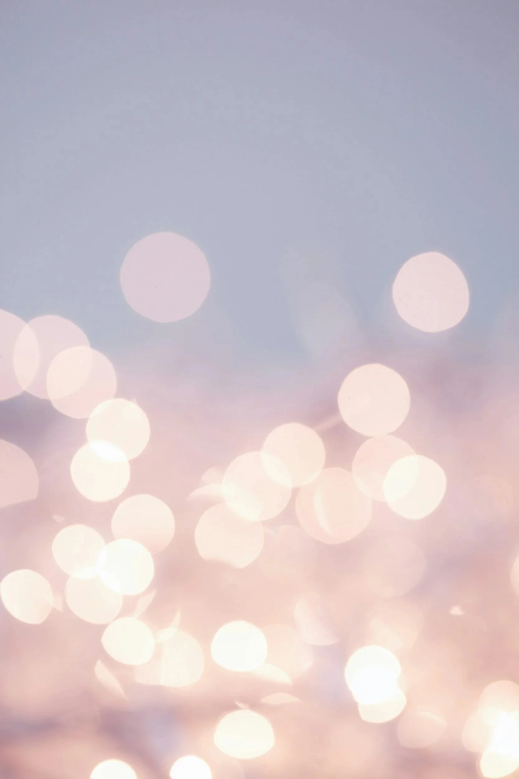 Blurred image of colorful bokeh lights in pastel shades of pink, purple, and white.