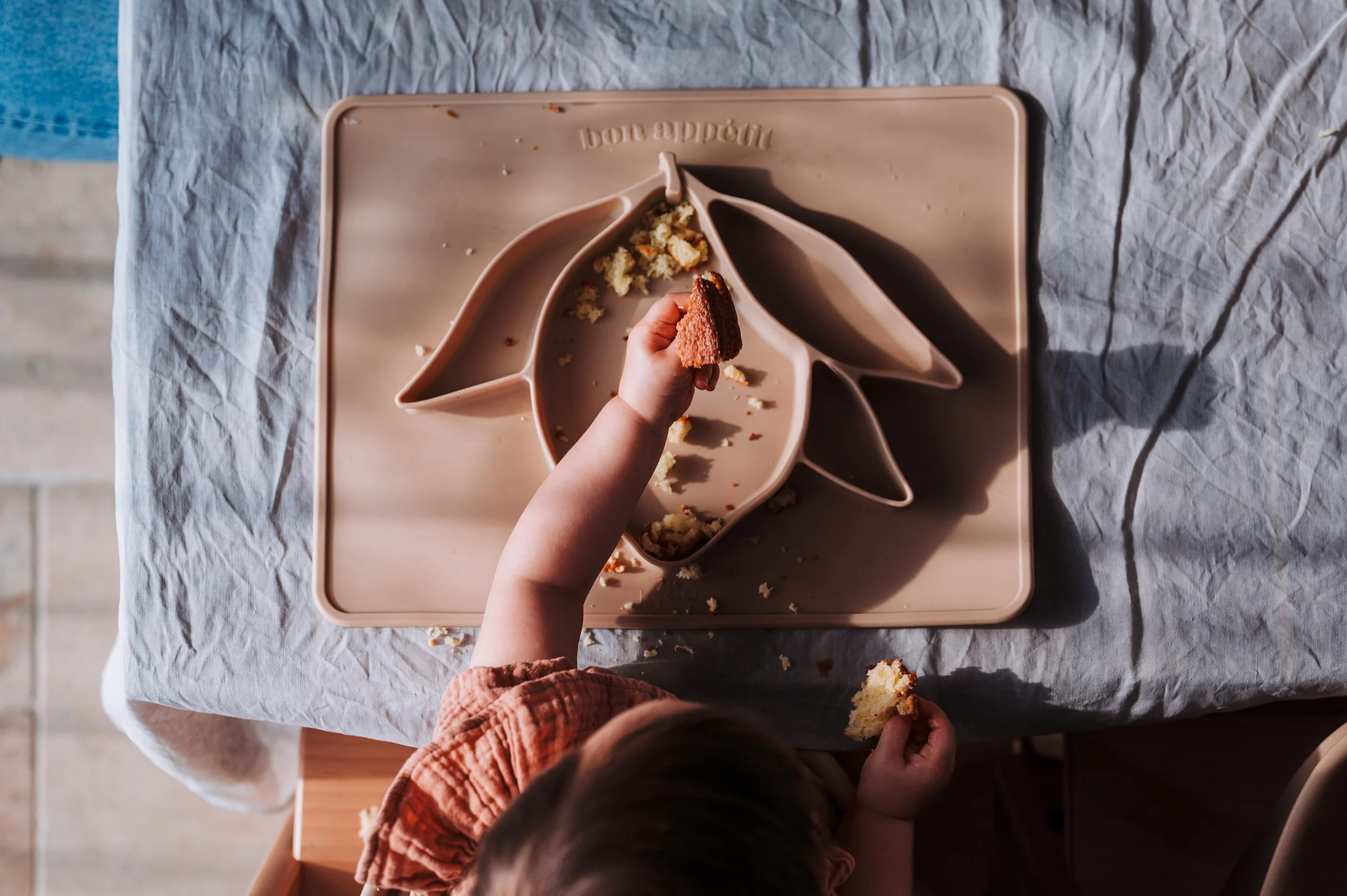 Gâteau de style gâteau au citron ou à la vanille en forme de licorne sur une table recouverte d'un tissu blanc. Quelqu'un enfonce une bouchée de gâteau dans la bouche de l'enfant, qui porte un pull marron.