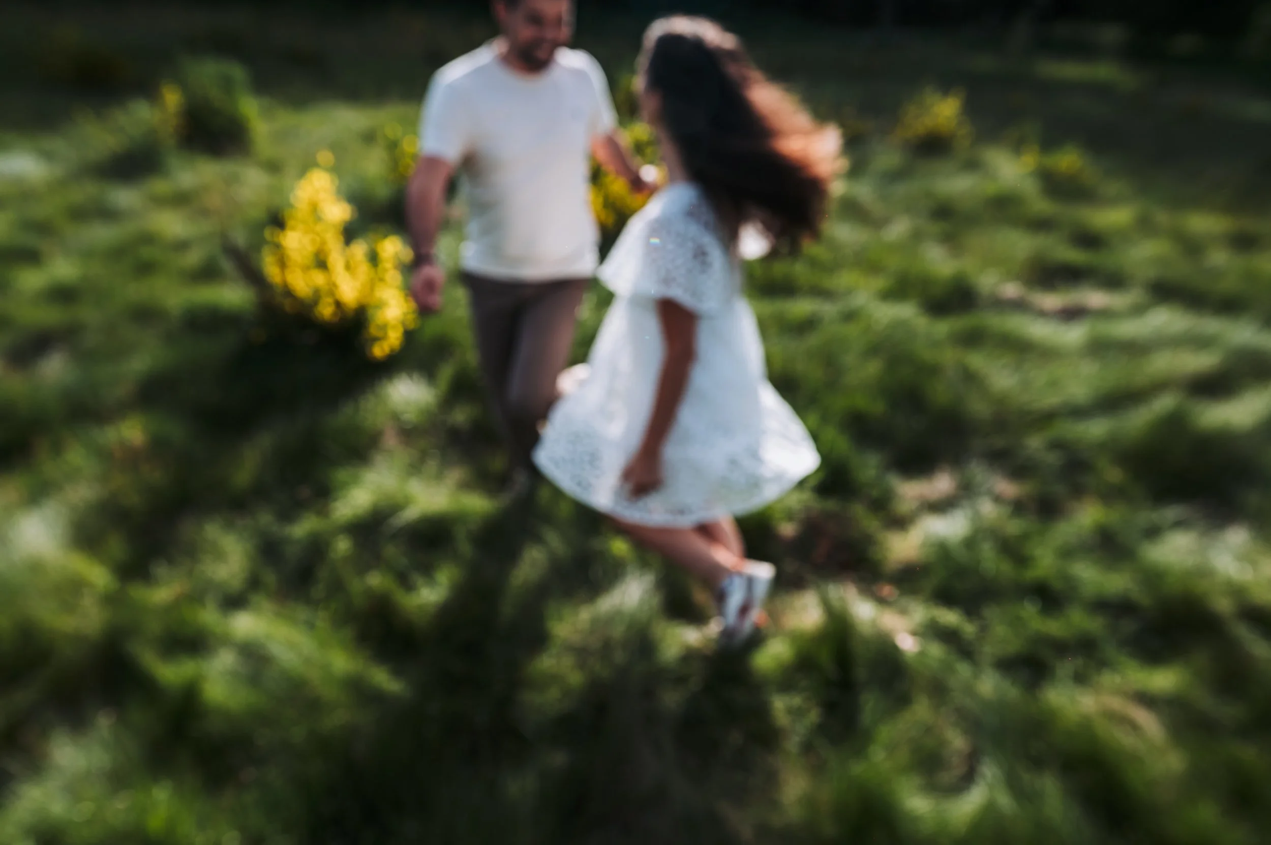 une fille en robe blanche et un garçon en t-shirt blanc marchant dans un champ ensoleillé, floue, arrière-plan verdoyant.