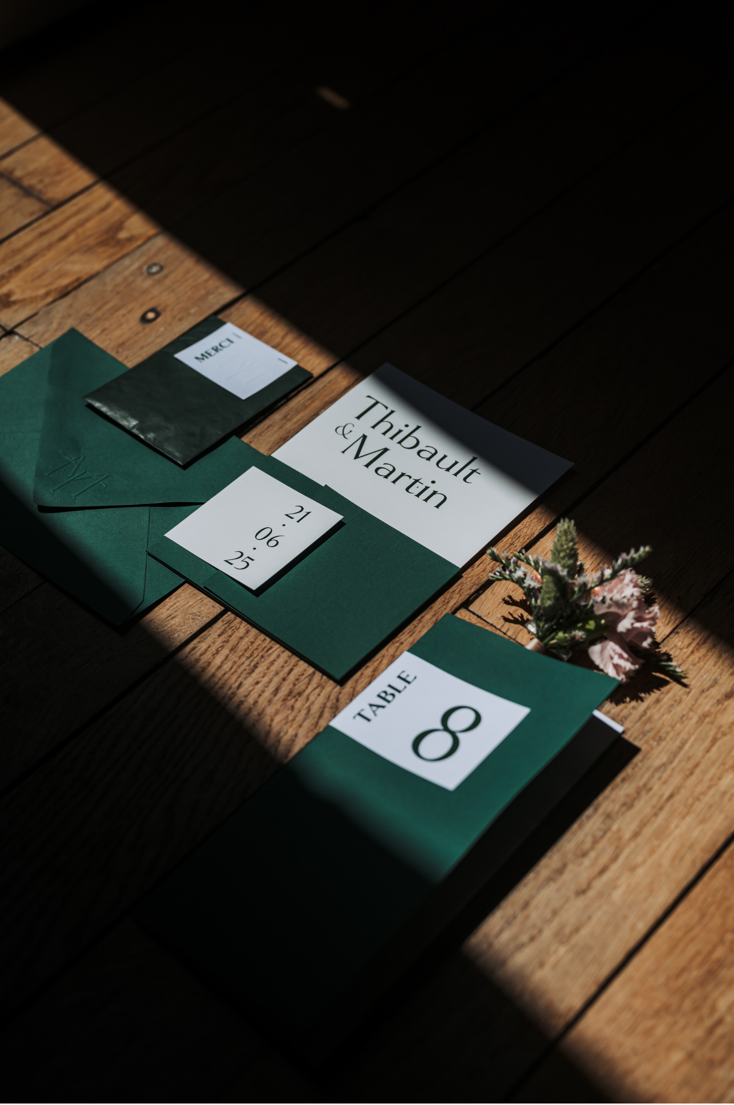 Décor de table de mariage ou d'événement avec un panneau indiquant le nom 'Thibault & Martin', une date, et des éléments de décoration florale, le tout posé sur un plancher en bois.