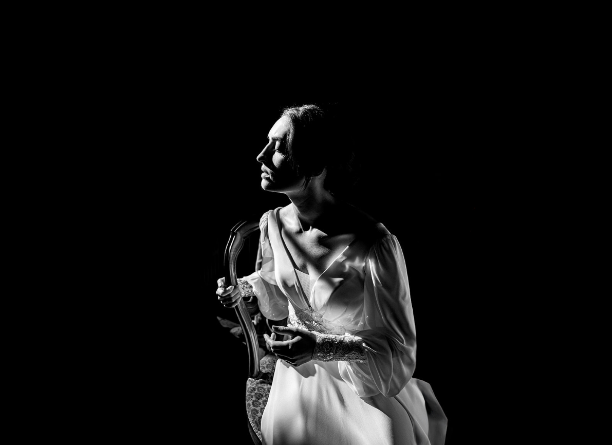 Une femme en robe élégante, regardant à gauche, dans un éclairage noir et blanc.