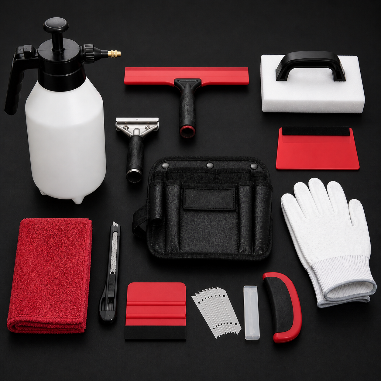 Cleaning supplies and tools arranged on a black surface, including a spray bottle, squeegee, scrub brush, gloves, red cloth, utility knife, razor blades, small container, cleaning sponges, and a black carrying bag.