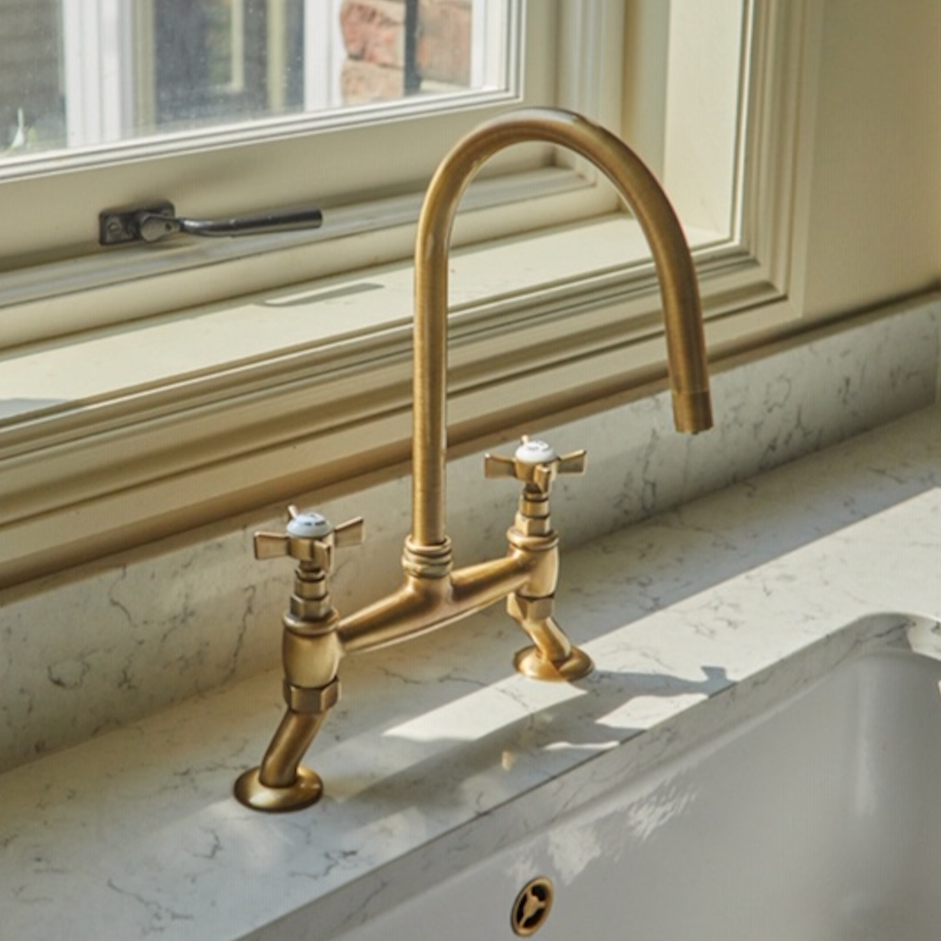 A bridge mixer from APC's Majestic Collection on a marble countertop, next to a window.