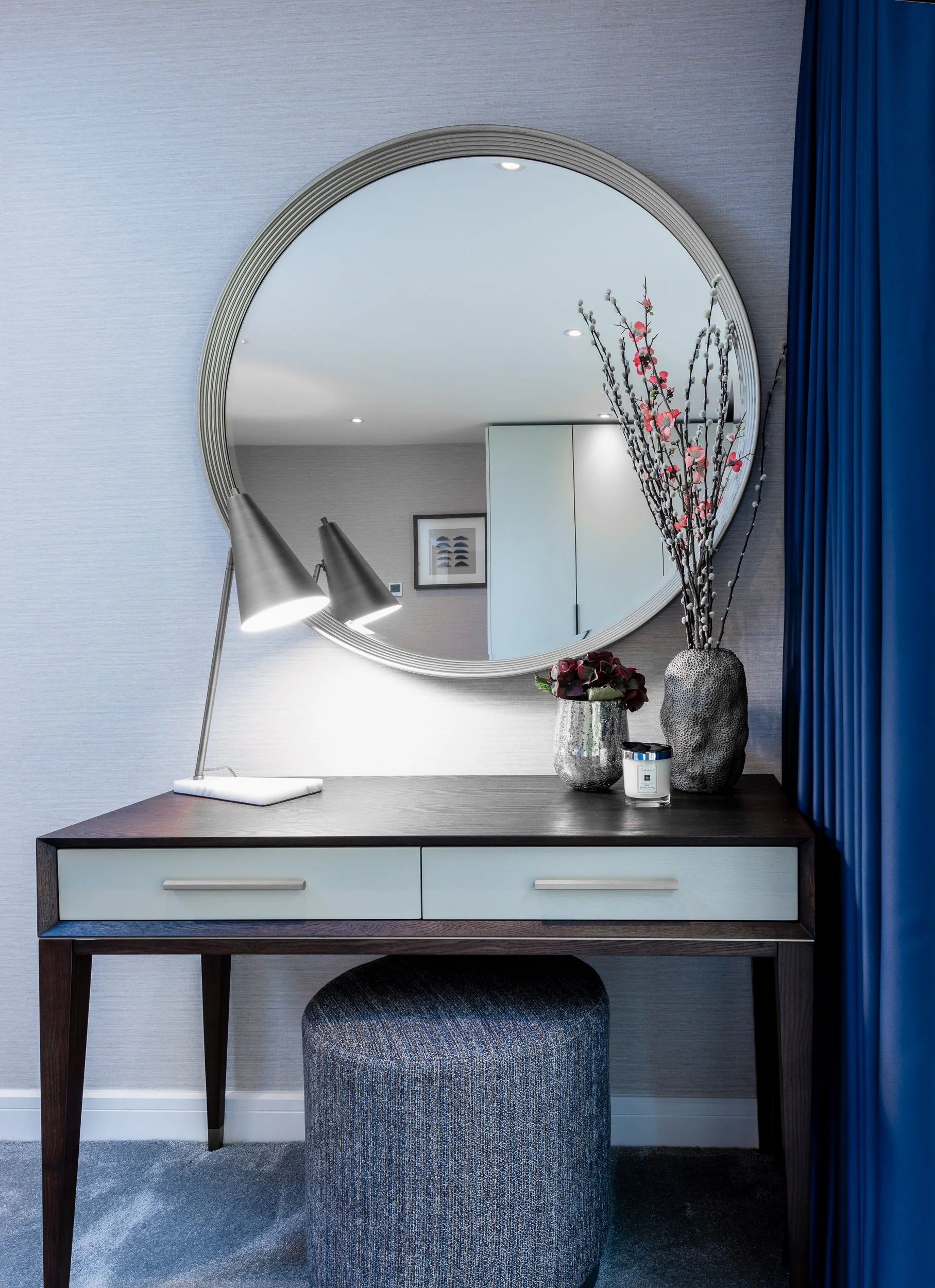 Contemporary bedroom dressing table with round mirror, upholstered stool and decorative styling details.