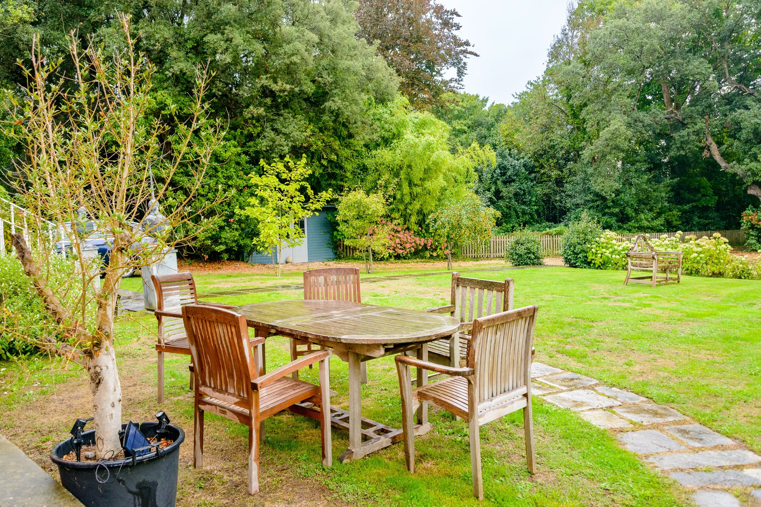 Garden seating area at The Pink House in Bembridge, with wooden table and chairs set within the lawn and surrounding trees.