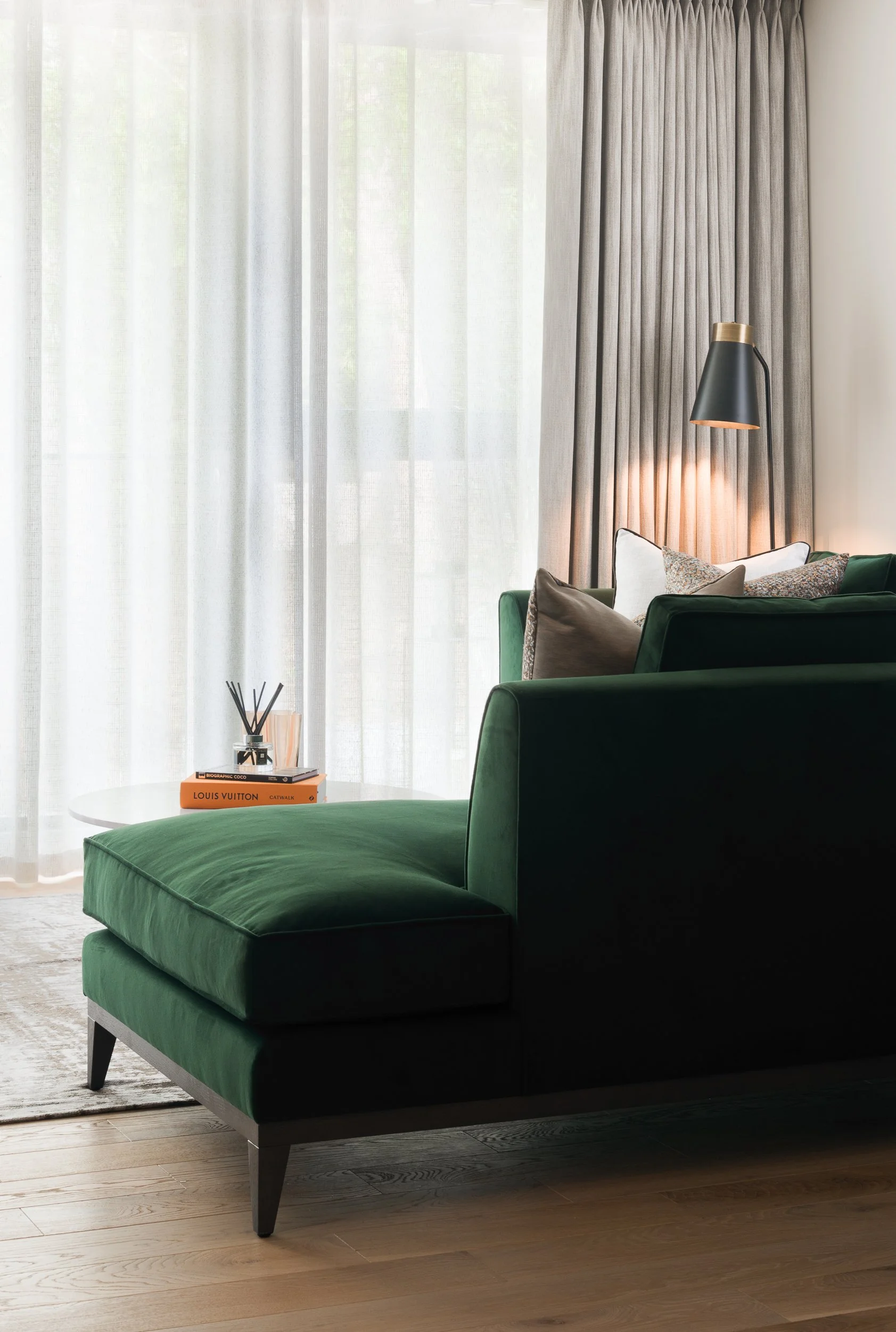 Contemporary lounge corner featuring dark teal chaise seating, floor lamp and full-height window treatments.