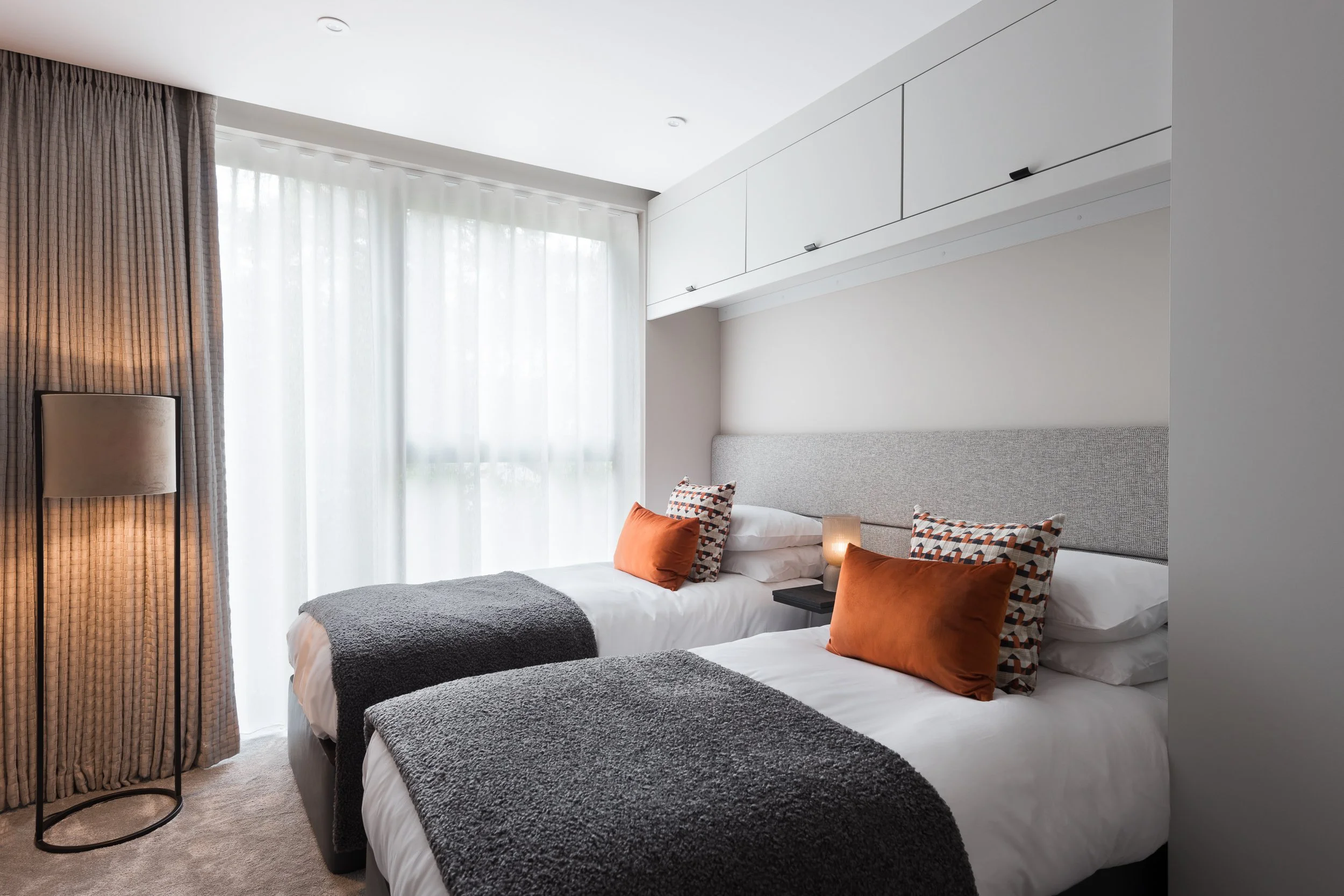 Modern guest bedroom with upholstered headboard, soft furnishings, fitted storage and contemporary styling.