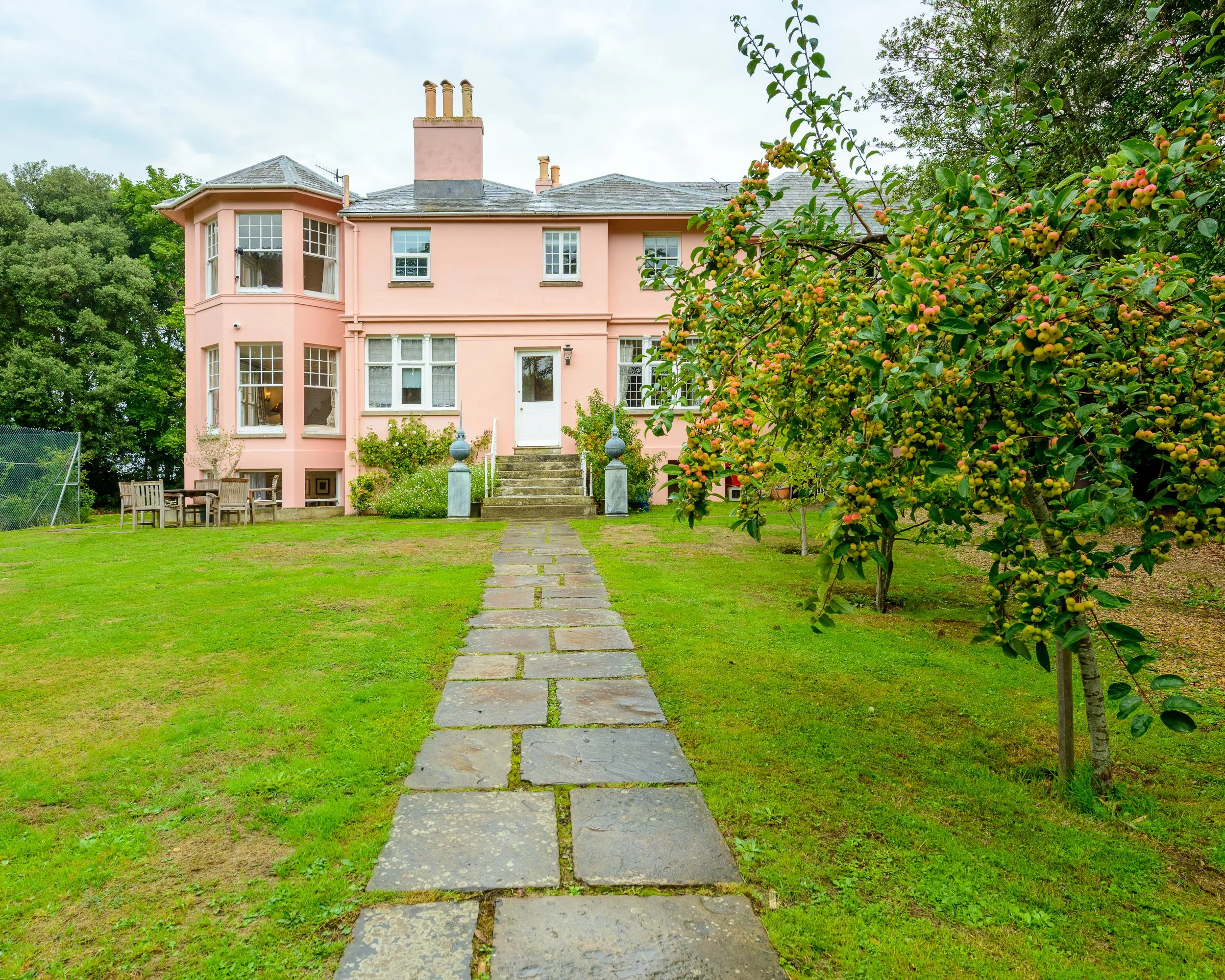 Exterior view of The Pink House in Bembridge, Isle of Wight, showing the pink period property, garden path and surrounding greenery.