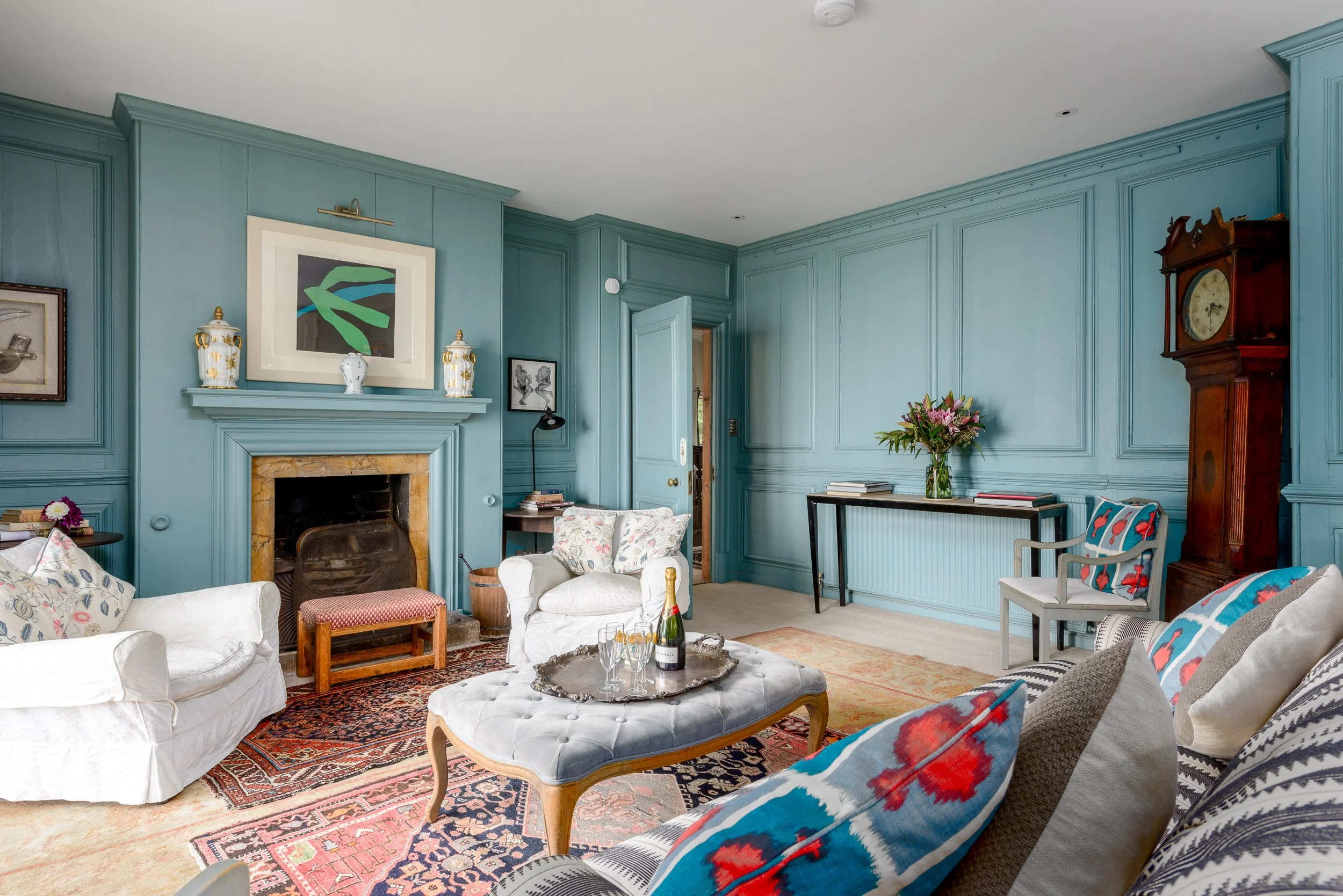 Blue sitting room at The Pink House with fireplace, traditional furniture, antique clock, patterned rugs and soft furnishings.