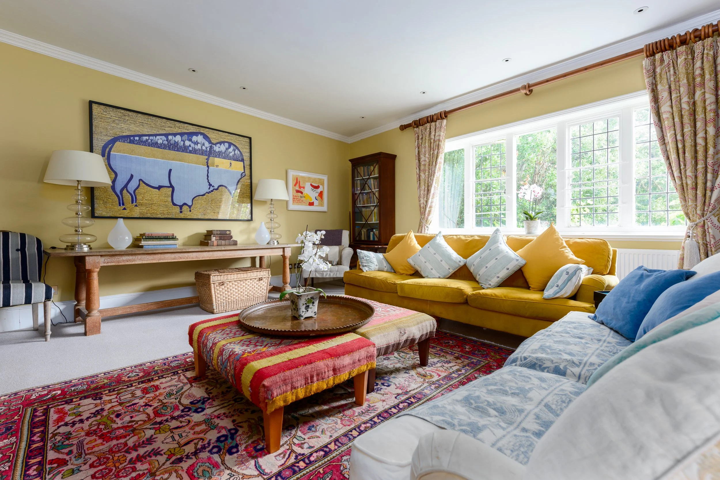 Yellow sitting room at The Pink House, featuring a mustard sofa, patterned rug, large artwork, antique furniture and bright window light.