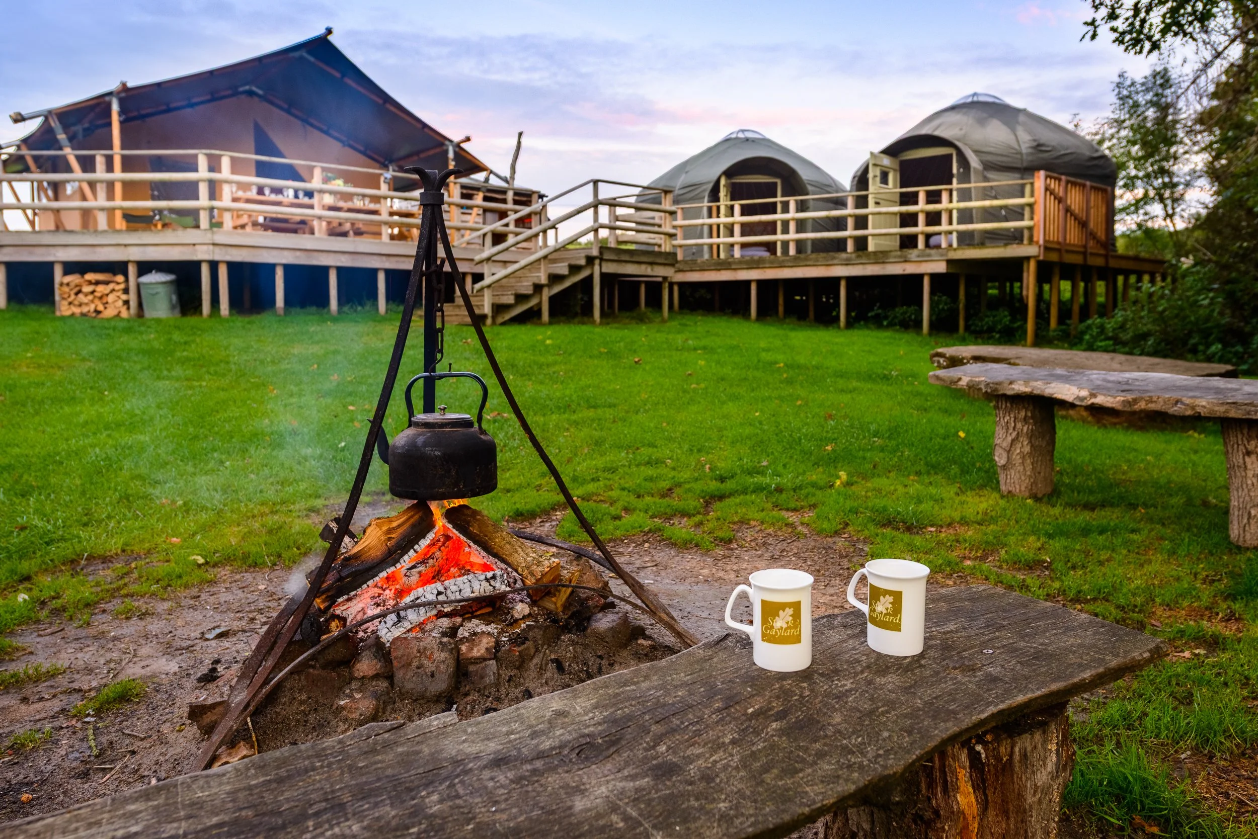 Firepit scene at Stock Gaylard glamping site, with safari tents and outdoor seating in the background.