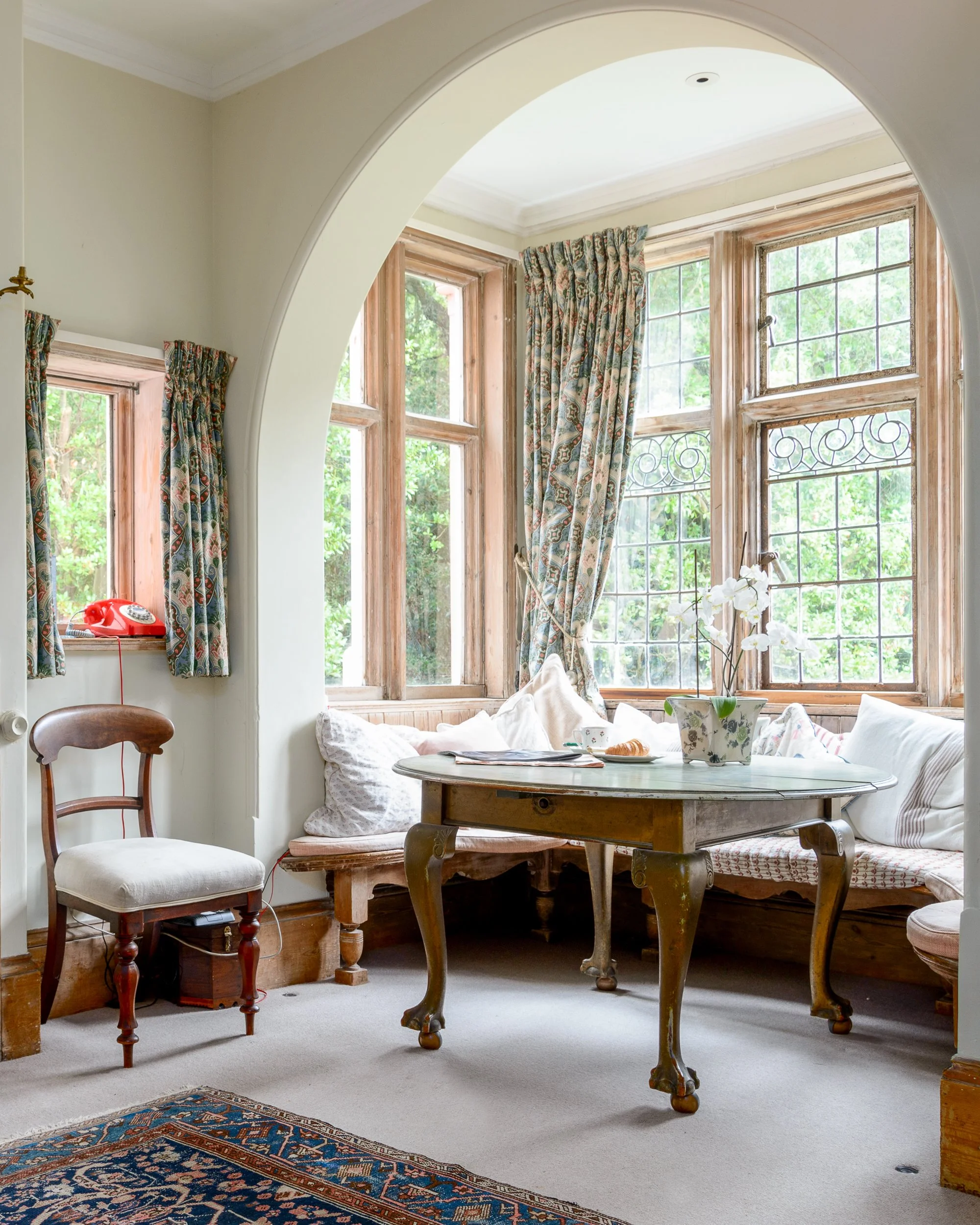 Dining area at The Pink House with a curved bay window, antique table, upholstered seating and period interior details.