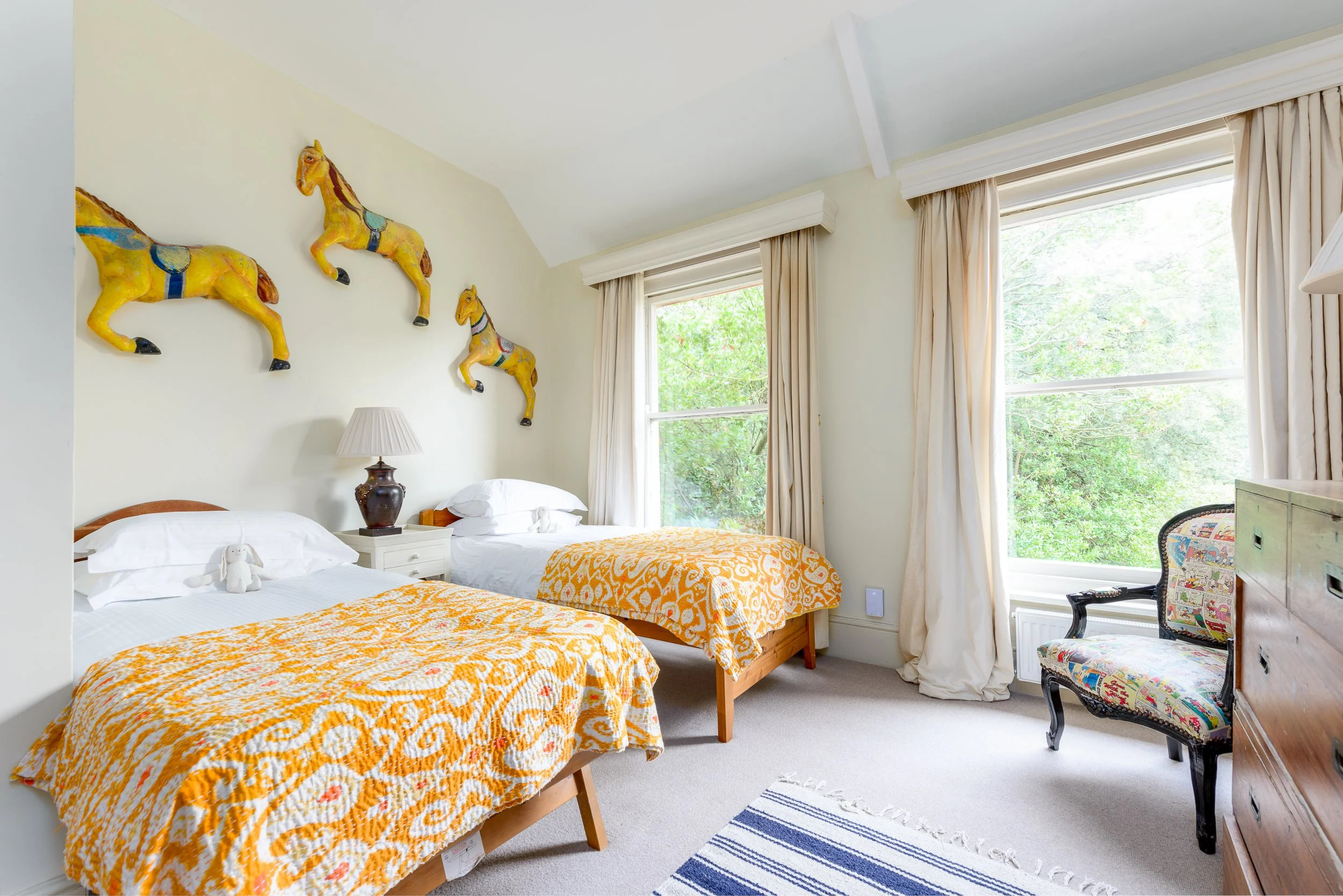 Twin bedroom at The Pink House in Bembridge, featuring yellow horse artwork, twin beds, patterned bedspreads and traditional furniture.
