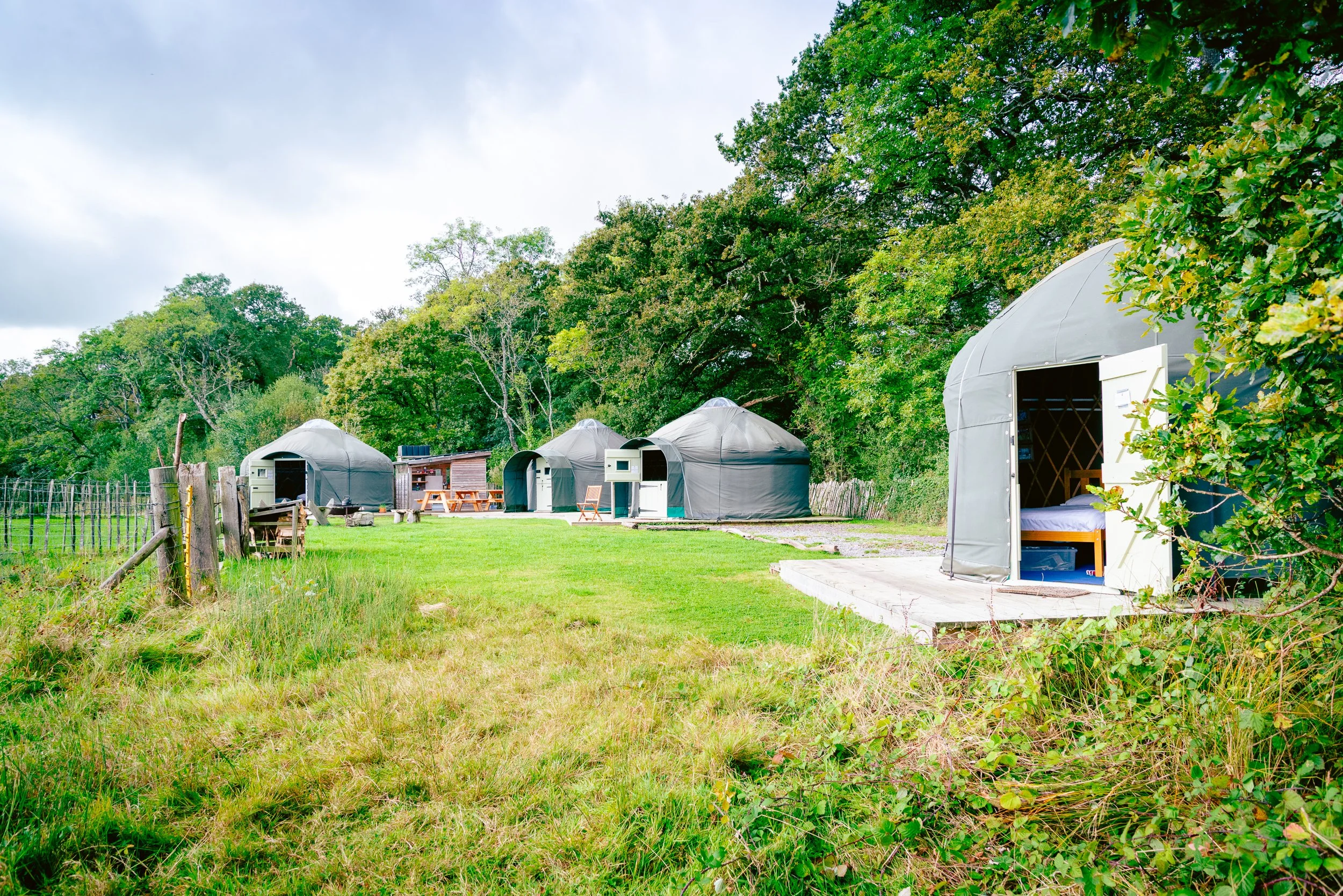 Wide view of Stock Gaylard glamping site in the Dorset countryside, showing yurts, outdoor seating and open fields.