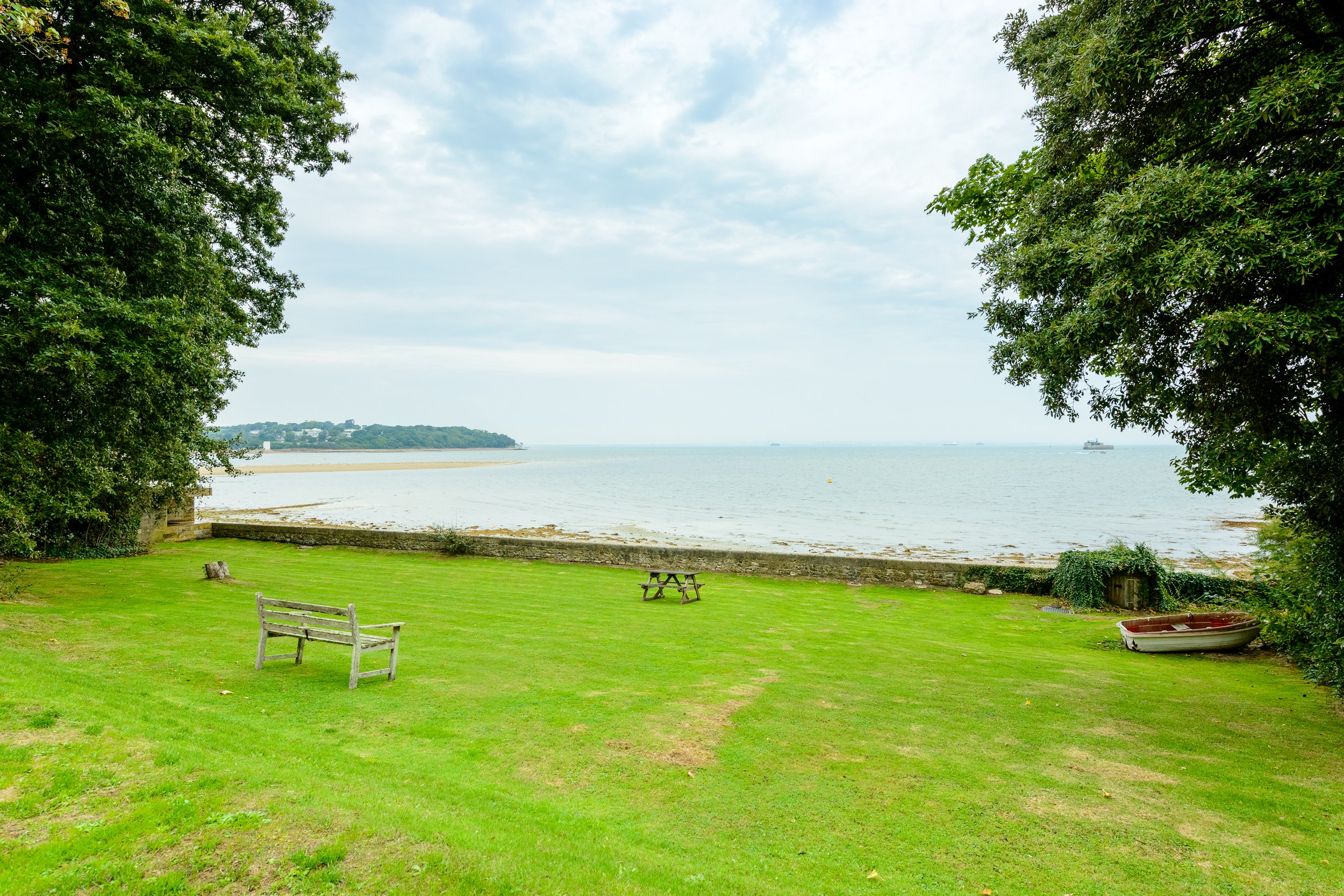 Coastal garden view from The Pink House in Bembridge, showing the lawn, seating area and sea beyond.