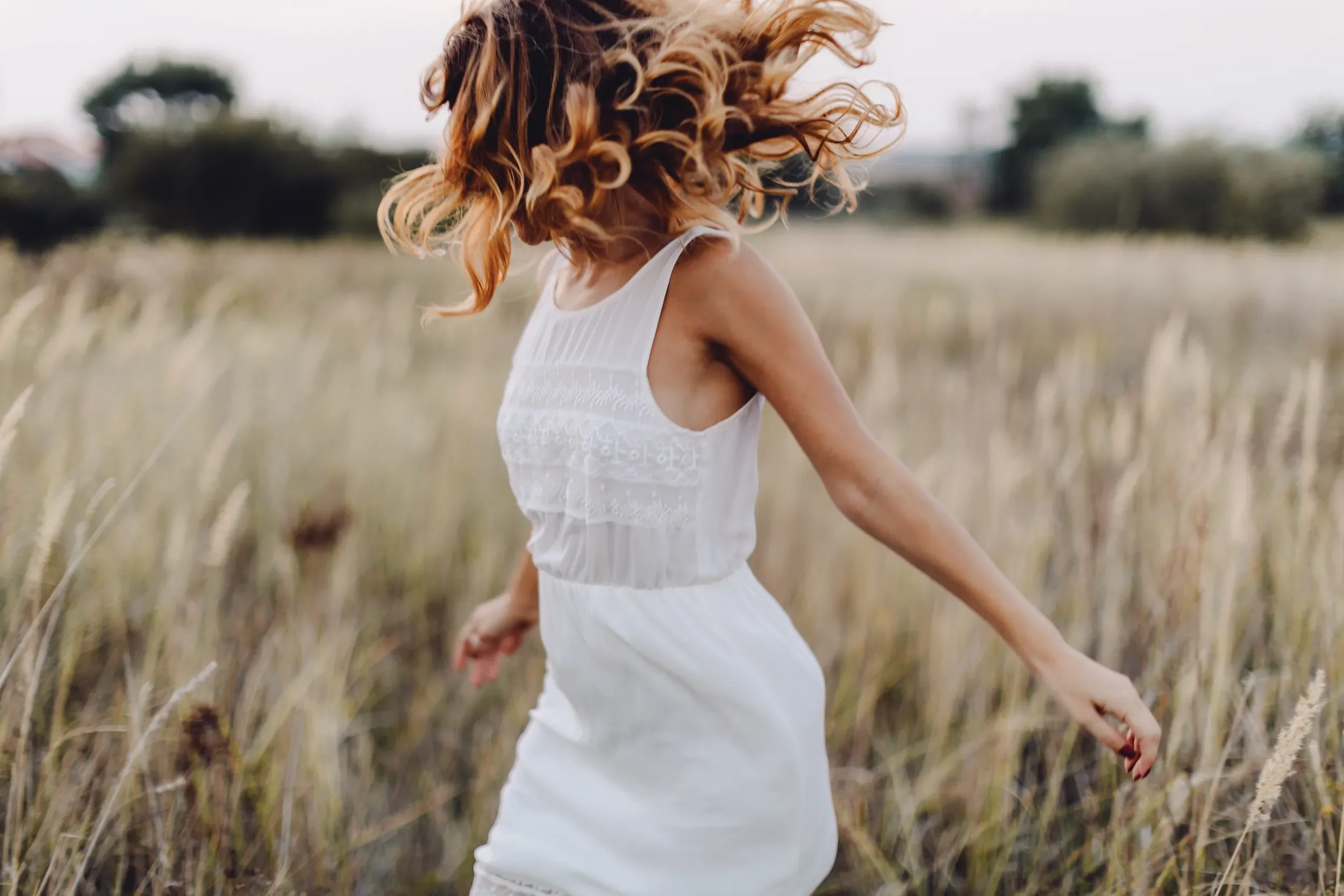 Woman with bouncy, natural-looking waves in a sunlit field, showcasing healthy, styled hair from Albert Fields salon in Goring-on-Thames.