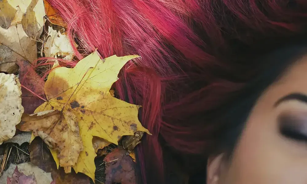 Close-up of vibrant red hair against autumn leaves, styled with bold colour at Albert Fields salon