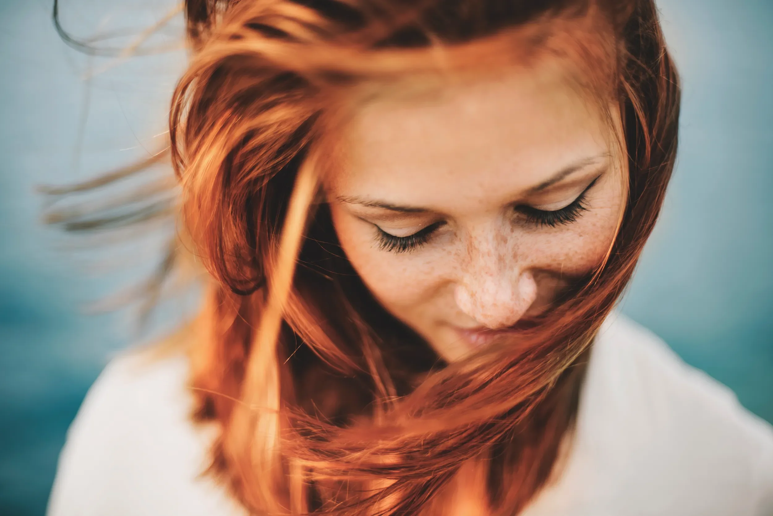 Close-up of a young woman with long red hair gently blowing in the wind, styled with a natural glossy finish at Albert Fields salon