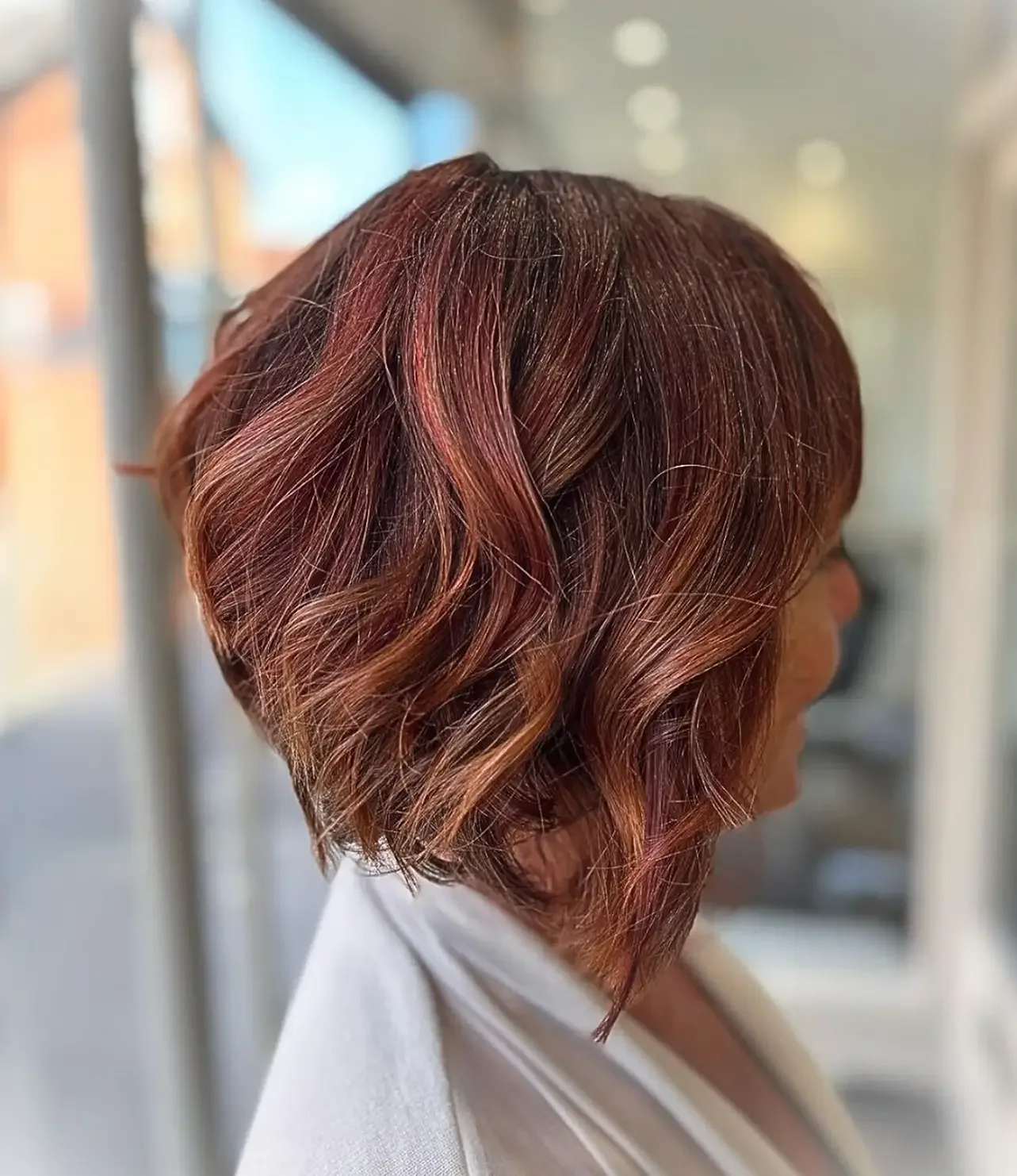 Side view of a woman with short, wavy, auburn-colored hair cut at Albert Fields