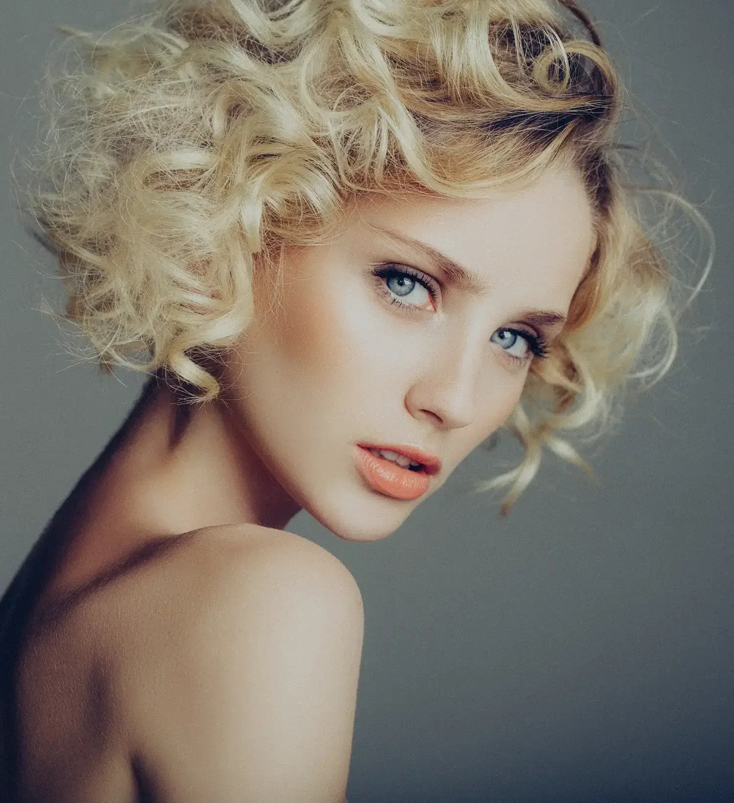 Close-up portrait of a woman with short blonde curls, styled in a modern textured look at Albert Fields salon