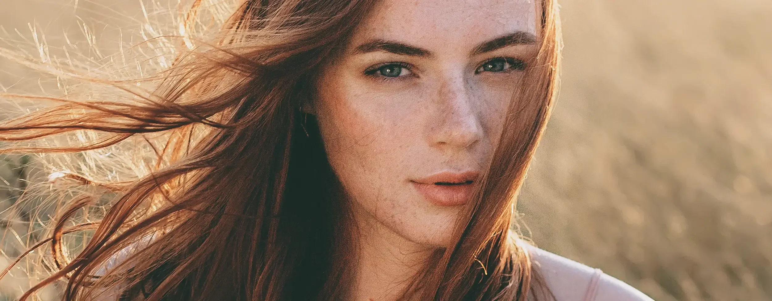 Portrait of a woman with flowing auburn hair in natural sunlight, styled with a glossy finish from Albert Fields salon