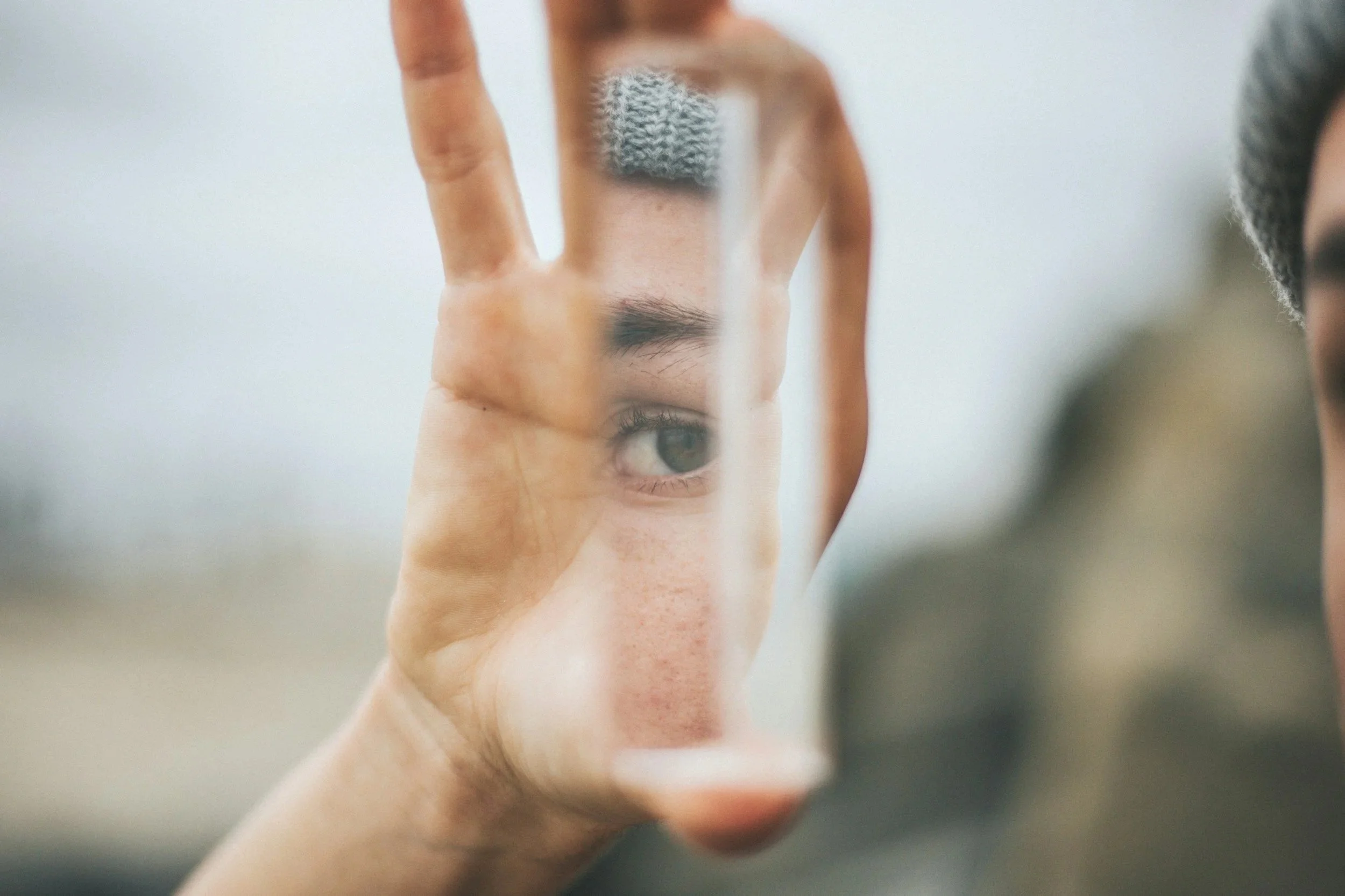 A person looking at a mirror that reflects their eye, hand, and part of their face, creating a layered effect.