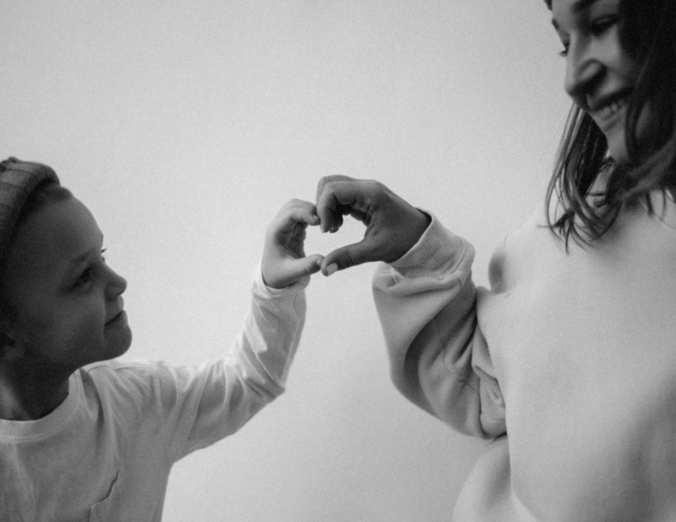 Una persona adulta y un niño formando un corazón con sus manos.