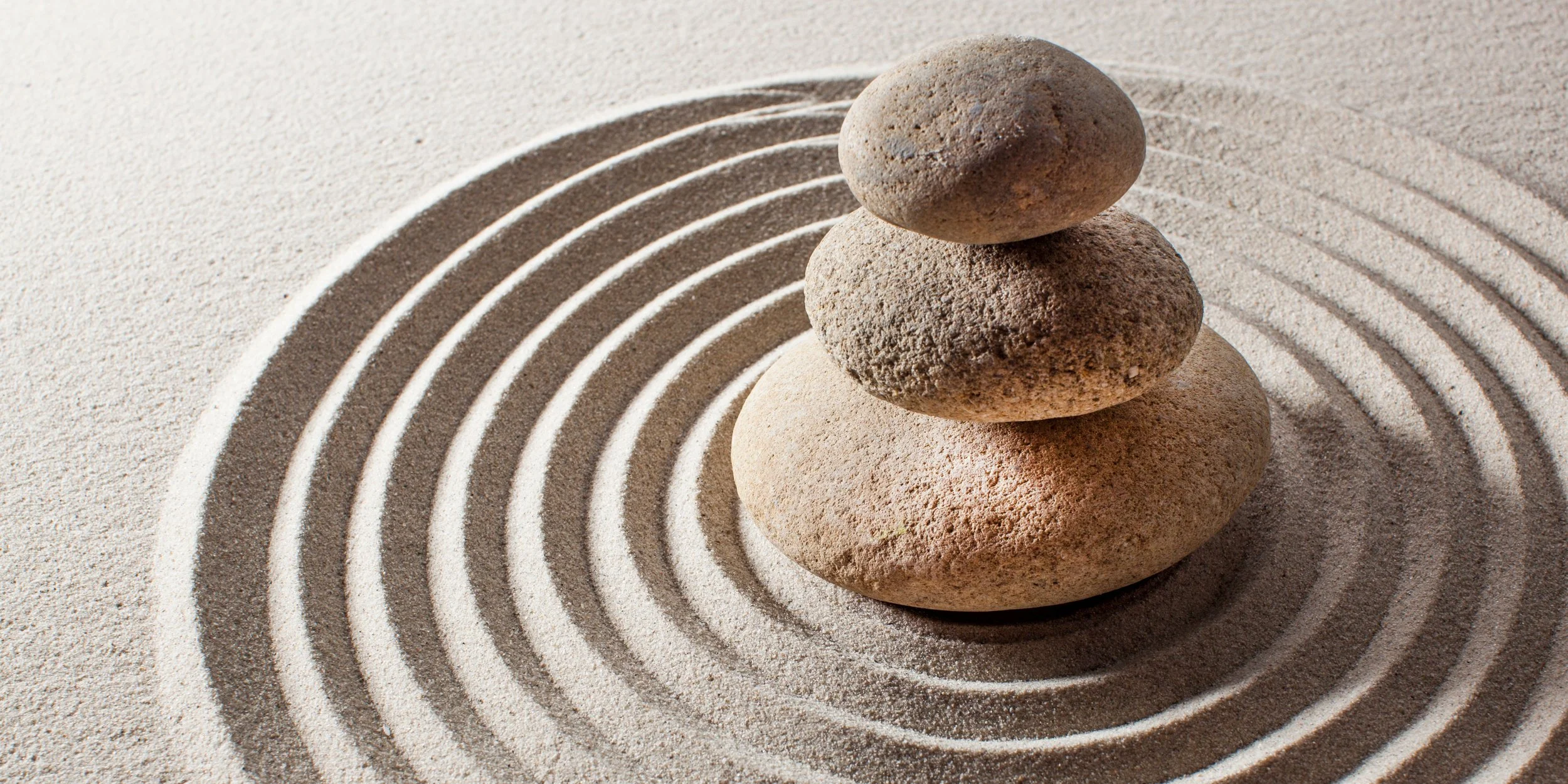 Piedras equilibradas sobre arena con ondas concéntricas en un jardín zen.