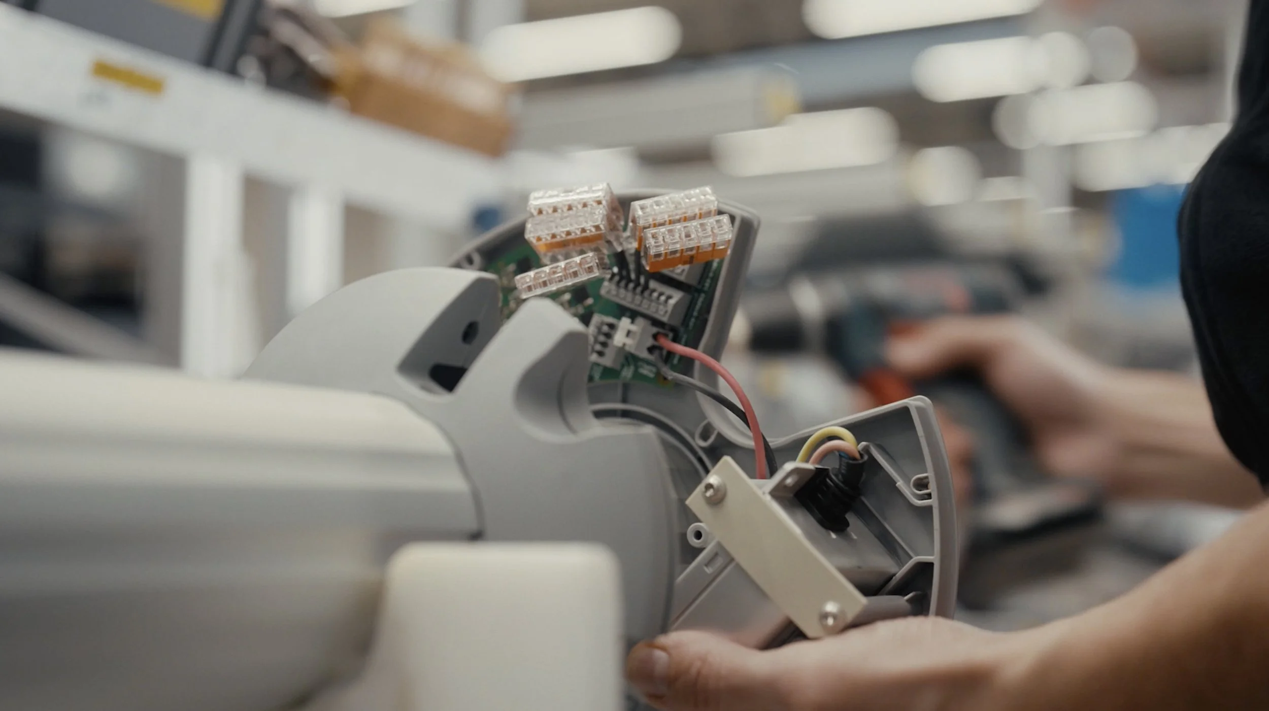 Hand arbeitet an einer elektrischen Baugruppe mit Kabeln und Steckverbindungen in einem technischen Arbeitsumfeld.