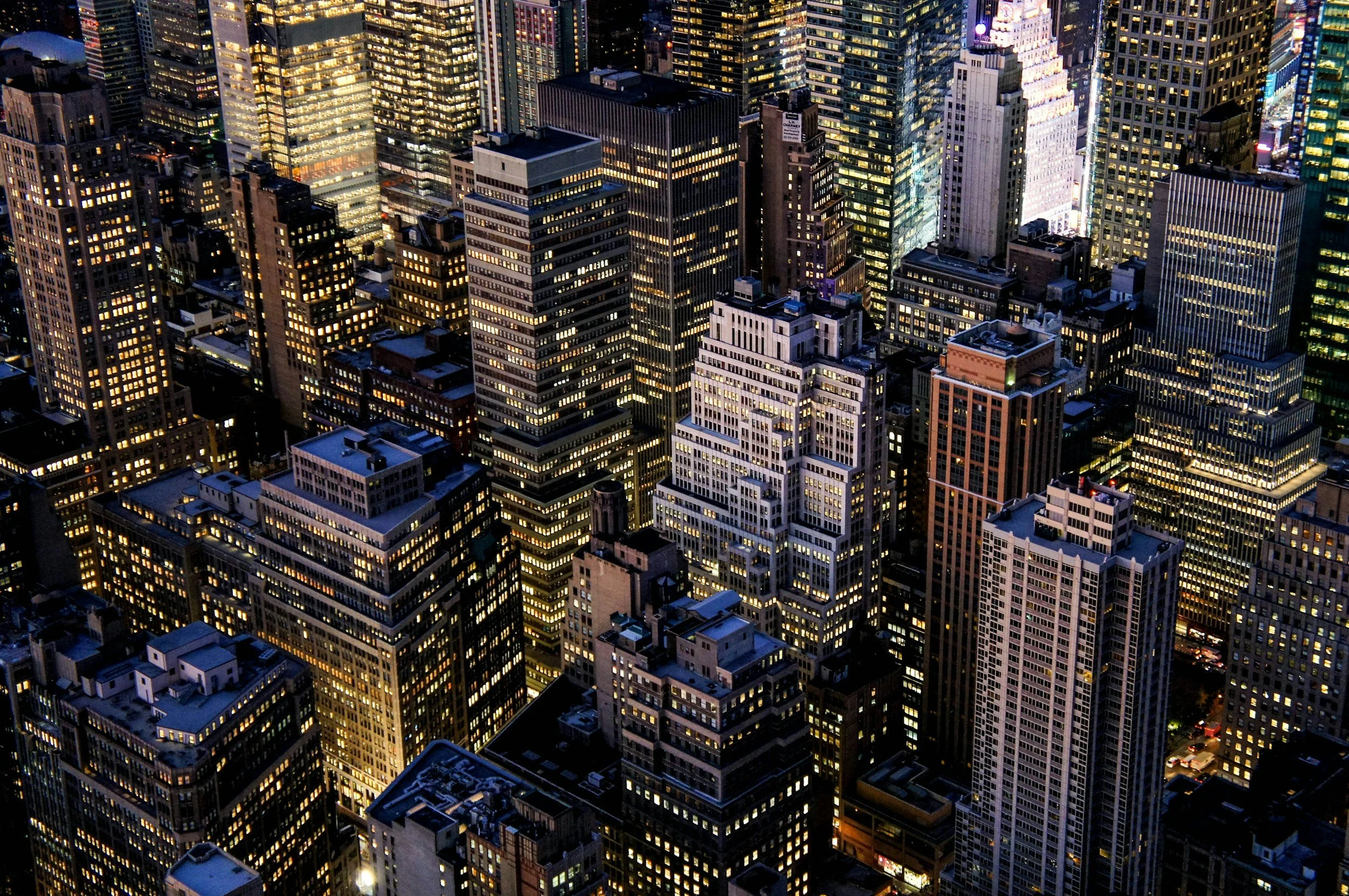 Aerial view of a cityscape at night with numerous high-rise buildings illuminated and traffic on the streets below.
